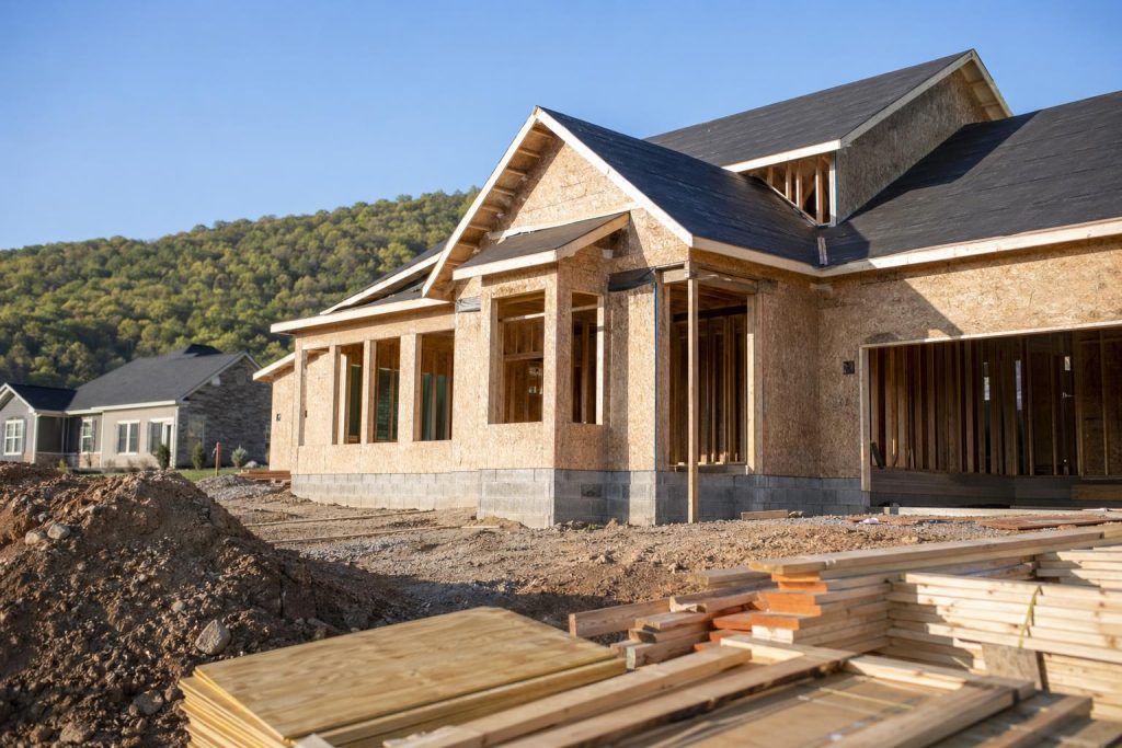 A new residential house in the early stages of construction with wooden framing and exterior walls partially complete on a hillside lot.